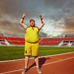 Fat man in sportswear shouts raised hands up standing in the stadium.